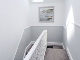A stairway with a white banister and grey carpet and a painting of boats on the wall at Dolawen Bach in Conwy