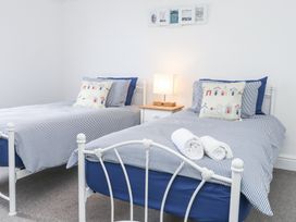 A bedroom with two twin beds, striped bedding, a nightstand with a lamp, and framed pictures on the wall at Dolawen Bach in Conwy