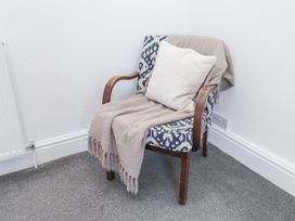 A patterned armchair with wooden arms a beige throw and a cushion in a carpeted corner at Dolawen Bach in Conwy