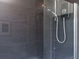 A shower area with gray tiled walls and a handheld showerhead at Dolawen Bach in Conwy