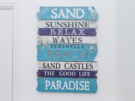 A decorative wall sign with beach themes and words like sand sunshine relax waves beach and paradise at Dolawen Bach in Conwy