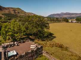 An outdoor deck with seating, a hot tub, and a barbecue grill overlooking a grassy field with trees and hills in the background at Leathes Head Country House Borrowdale near Keswick