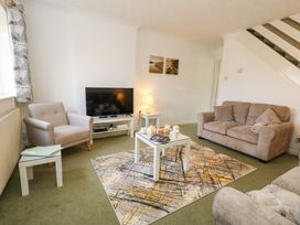 A living room with a sofa an armchair a television on a stand a coffee table with teacups and snacks a lamp on a side table and two wall pictures at Dorset Explorers in Bournemouth