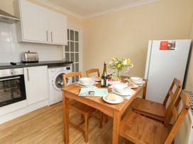 A kitchen with a wooden dining table set for four with bowls bread and wine next to white cabinets and a refrigerator at Dorset Explorers in Bournemouth