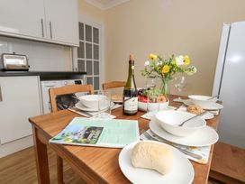 A kitchen dining table set with bowls, plates, a bottle, glasses, bread, fruit bowl, and flowers at Dorset Explorers in Bournemouth