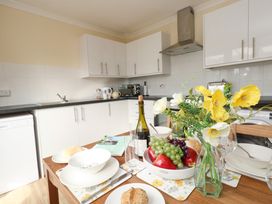 A kitchen with white cabinets a dining table with bowls plates glasses a bowl of fruit and a vase with yellow and white flowers at Dorset Explorers in Bournemouth
