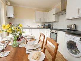 A kitchen with white cabinets appliances and a wooden dining table set with bowls bread and flowers at Dorset Explorers in Bournemouth