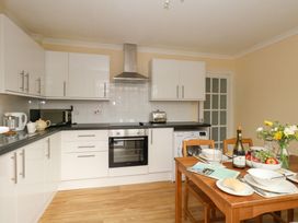 A kitchen with white cabinets black countertops a washing machine and a wooden dining table with dishes fruits and flowers at Dorset Explorers in Bournemouth