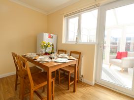 A dining area with a wooden table and four chairs set for a meal next to a refrigerator and a glass door leading to a sunroom at Dorset Explorers in Bournemouth