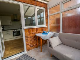 A small enclosed porch area with a gray sofa a folding table with books on it and a view into a kitchen with white cabinets in Dorset Explorers Bournemouth