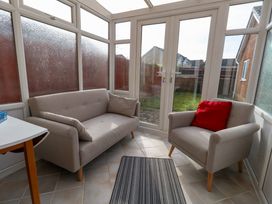 A conservatory with a sofa and armchair facing glass doors with garden view at Dorset Explorers in Bournemouth