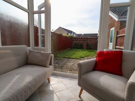 A sunroom with two armchairs and a view of a fenced backyard with grass at Dorset Explorers in Bournemouth
