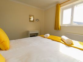 A bedroom with a bed covered in white and yellow linens two rolled towels on the bed a window with yellow curtains a small white desk a floor lamp and a small wall mirror at Dorset Explorers in Bournemouth