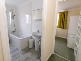 A bathroom with a bathtub shower sink and trash bin next to a bedroom with green carpet and yellow curtains at Dorset Explorers in Bournemouth