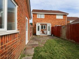 A backyard with a patio area and grass between two brick houses at Dorset Explorers in Bournemouth