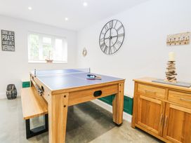 A game room with a ping pong table two paddles balls a bench wooden cabinet with a candle and a large wall clock at The Ivy in Happisburgh East Anglia