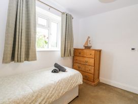 A bedroom with a single bed with rolled towels on it a wooden chest of drawers with a model ship on top and a window with curtains at The Ivy in Happisburgh East Anglia