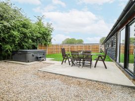 A backyard with wooden patio furniture and a hot tub next to a gravel area at The Ivy in Happisburgh East Anglia