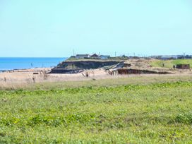 A grassy field leading to a sandy beach with houses on a hill and the sea in the background at The Ivy in Happisburgh East Anglia