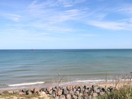 A beach with rocks in the foreground and a red boat on the sea under a blue sky at The Ivy in Happisburgh East Anglia