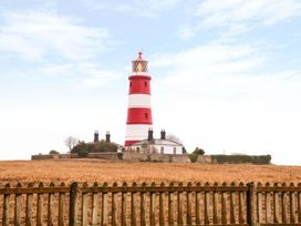 A red and white striped lighthouse with attached buildings behind a wooden fence in a field at The Ivy in Happisburgh East Anglia