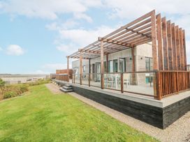 A wooden deck with a pergola and outdoor dining furniture next to a grassy area at Hepworth in Portreath