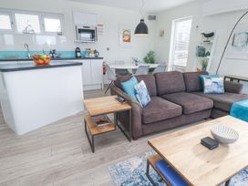 A living room with a gray couch and a wooden coffee table next to a kitchen with white cabinets and a dining table at Hepworth in Portreath