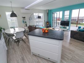An open living space with a kitchen island fruit bowl dining table chairs gray couch wood stove and television at Hepworth in Portreath