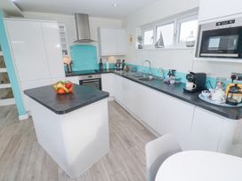 A kitchen with white cabinets black countertops a kitchen island with a fruit basket and appliances at Hepworth in Portreath