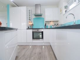 A kitchen with white cabinets black countertops a stainless steel oven and a blue backsplash at Hepworth in Portreath