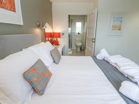 A bedroom with a bed with white and grey bedding two pillows with orange flowers a door leading to a bathroom with a toilet and shower at Hepworth in Portreath