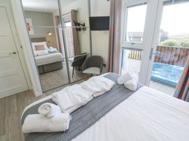 A bedroom with a bed towels and robes a chair mirrored wardrobe a wall mounted tv and door leading to a deck with a hot tub at Hepworth in Portreath