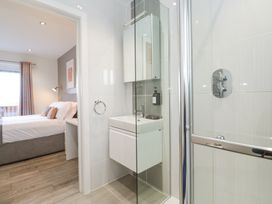A bathroom with a glass shower enclosure and a sink with a mirror cabinet next to a bedroom with a bed and window at Hepworth in Portreath