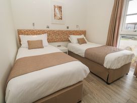 A bedroom with two single beds with beige throws and pillows a nightstand a framed picture on the wall and a window with curtains at Hepworth in Portreath