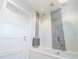 A bathroom with a white door a bathtub a glass shower screen and tiled walls