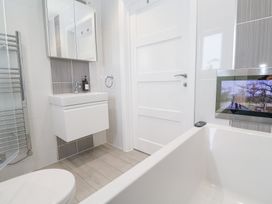 A bathroom with a white bathtub a wall-mounted television a white sink with mirror cabinet and a towel radiator at Hepworth in Portreath