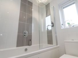 A bathroom with a bathtub shower combination a glass shower screen a window with a potted plant and a toilet at Hepworth in Portreath
