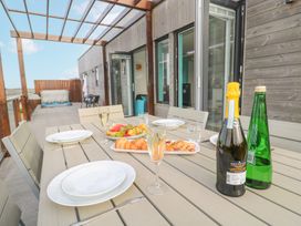An outdoor dining table with plates glasses pastries fruit and bottles on a terrace with wooden walls at Hepworth in Portreath