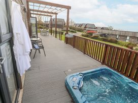 An outdoor deck with a hot tub tables chairs and bathrobes hanging on the wall at Hepworth in Portreath