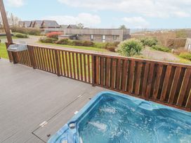 A wooden deck with a hot tub and metal barbecue overlooking modern buildings and greenery at Hepworth in Portreath