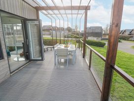 A wooden deck with a dining table and chairs under a pergola next to a house at Hepworth in Portreath