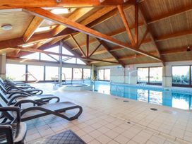 An indoor swimming pool with lounge chairs and a hot tub under a wooden beamed ceiling at Hepworth in Portreath