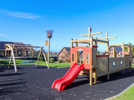 A playground with a wooden ship structure with a red slide and wooden swing set at Hepworth in Portreath
