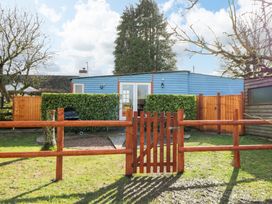 A blue wooden house with white double doors behind a wooden fence and gate with green hedges in front at Shed Your Blues Brilley near Kington