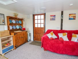 A living room with a red covered sofa and patterned cushions next to a wooden cabinet with blue plates at Shed Your Blues Brilley near Kington