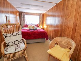 A bedroom with a bed covered with a red blanket two wicker chairs and wooden panel walls at Shed Your Blues in Brilley near Kington