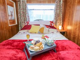A bedroom with a bed covered with red and white bedding and pillows a tray with breakfast items on the bed a painting of a deer on the wood paneled wall at Shed Your Blues Brilley near Kington