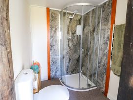 A bathroom with a toilet a corner shower with glass doors and stone effect walls at Shed Your Blues in Brilley near Kington