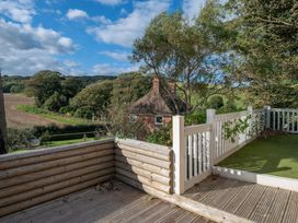 An outdoor wooden deck with white railings surrounded by trees and a house in the background at The Retreat Near Shorwell