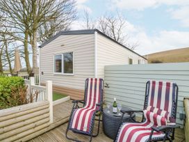 A deck with two striped lounge chairs and a small round table with a bottle and wine glasses outside a mobile home at The Retreat Near Shorwell